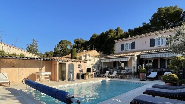 A pool area with lounge chairs, a poolside table, and a building in the background.
