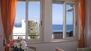 A room with a table, chairs, a vase of flowers, and a view of the sea through large windows. - House 100 meters from the sea Sardinia (SINISCOLA)