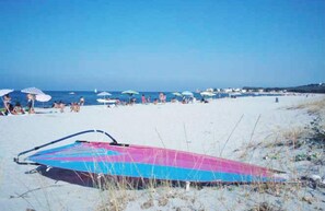 Ein Strand mit Menschen, Sonnenschirmen und einem bunten Drachen im Sand.