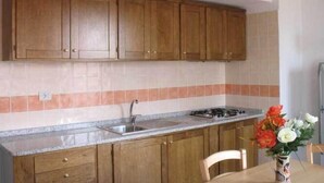A kitchen with wooden cabinets, a granite countertop, and a gas stove. - House 100 meters from the sea Sardinia (SINISCOLA)