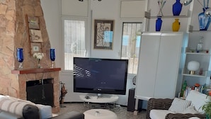 Ein Wohnzimmer mit Kamin aus Stein, einem großen Flachbildfernseher, Korbmöbeln und einem Bücherregal mit Dekoration.