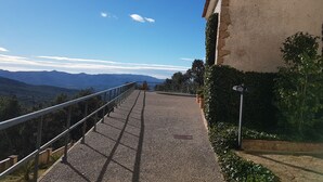 Ein gepflasterter Weg mit Metallgeländer, der zu einem Gebäude mit Ziegeldach und Blick auf ferne Berge führt.