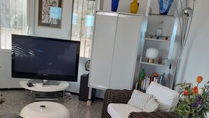 Ein Wohnzimmer mit Fernseher, Korbmöbeln, einem weißen Schrank und dekorativen Vasen.