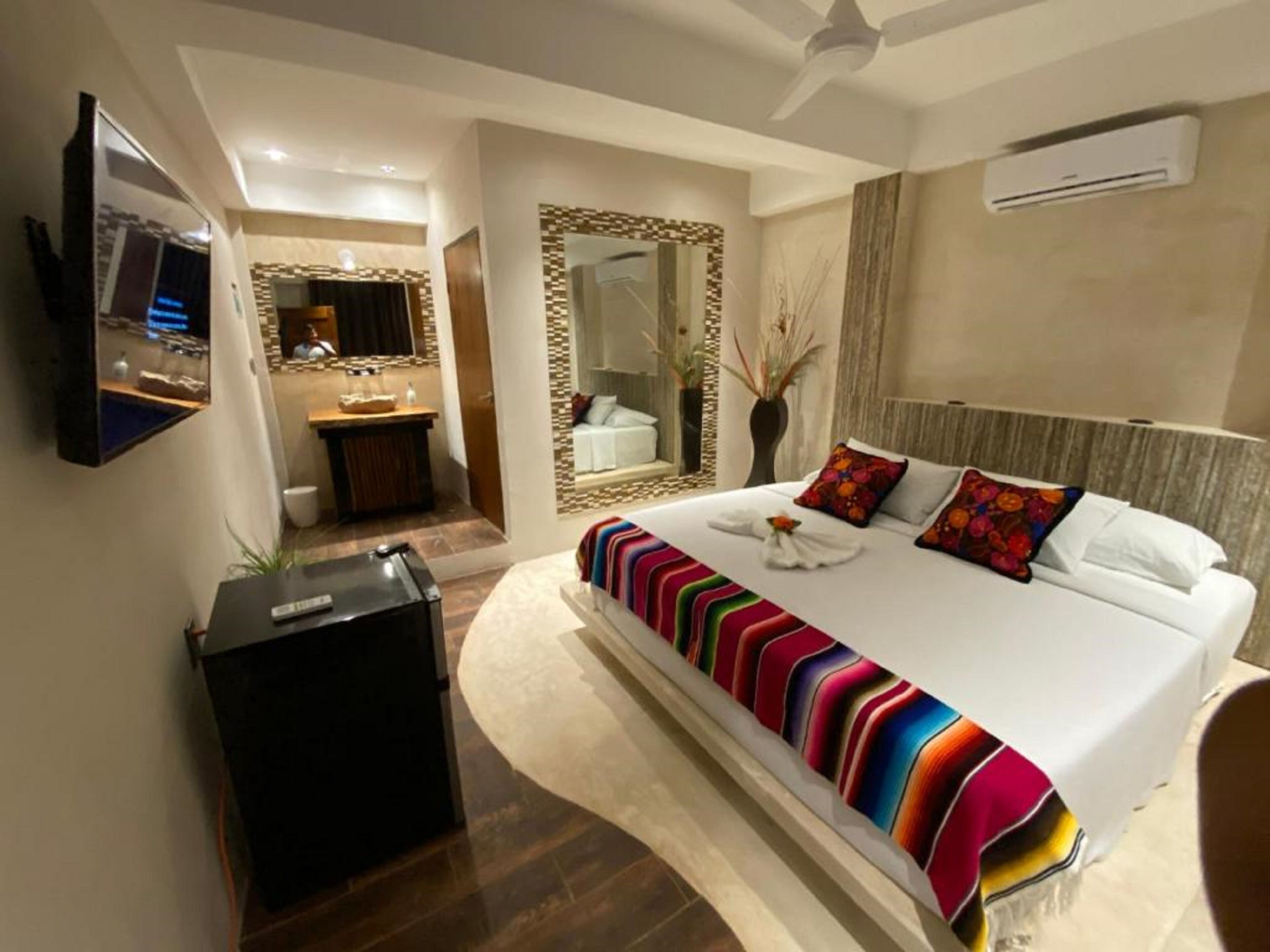 A modern hotel room with a large bed, a TV, a bathroom with a mirror, and an air conditioning unit.