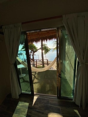 A room with a glass door leading to a deck with a hammock and a view of the sea. - Bahía Tolok (Isla Mujeres)