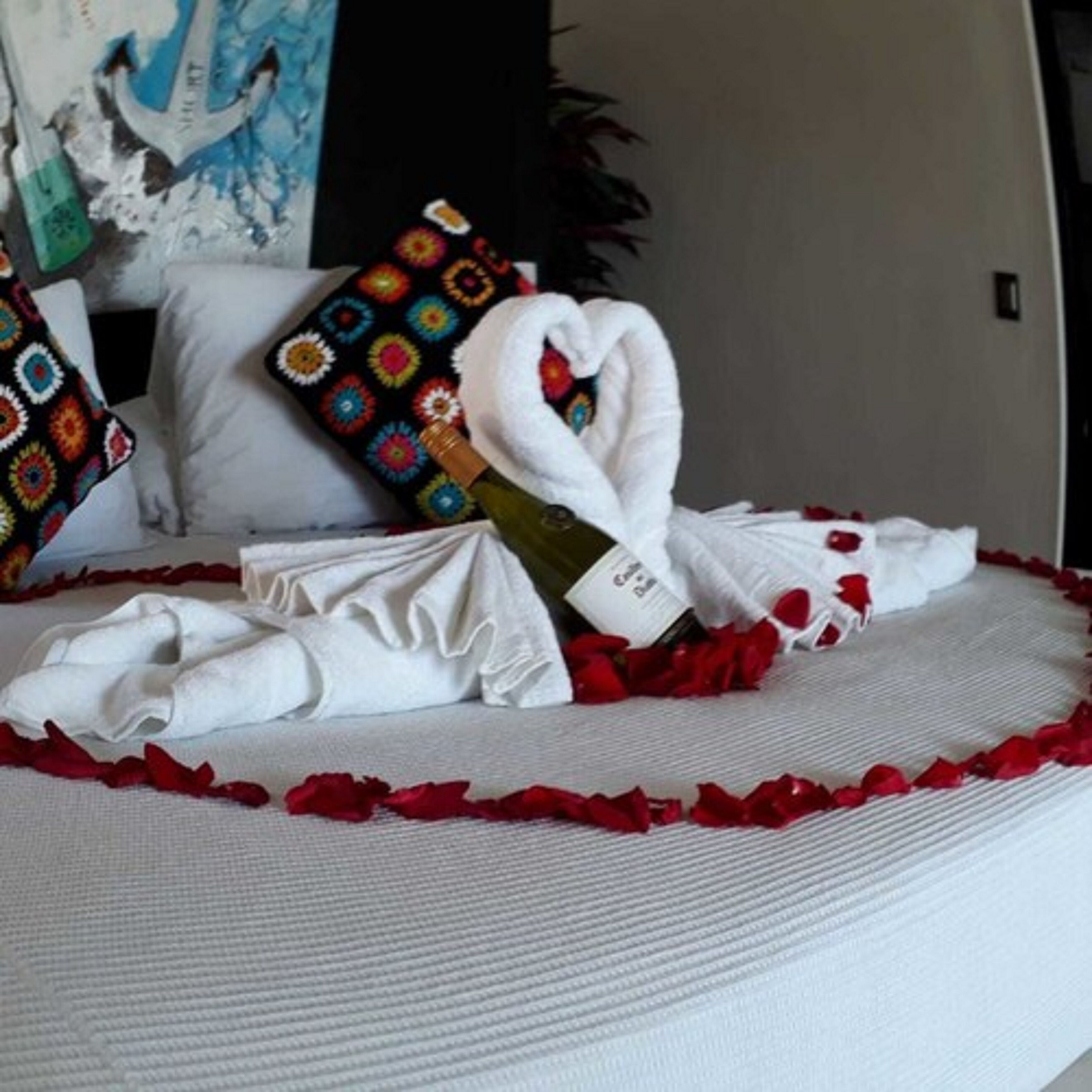 A neatly made bed with a heart-shaped towel, white pillows, and a colorful pillow with a geometric pattern.