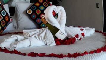 A neatly made bed with a heart-shaped towel, white pillows, and a colorful pillow with a geometric pattern.