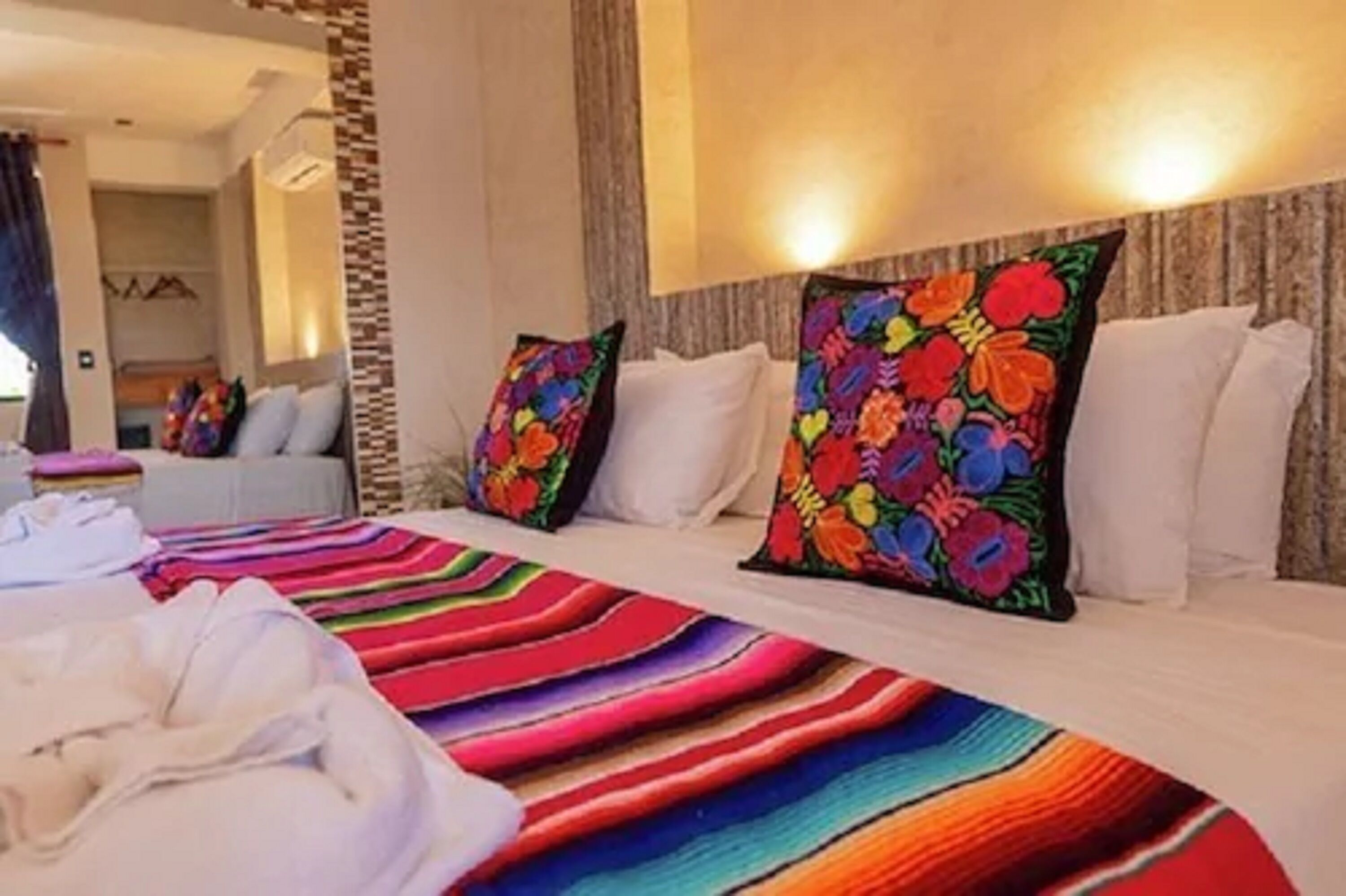 Una habitación de hotel con una cama, almohadillas de colores, una colcha a rayas y ropa de cama blanca impecable.