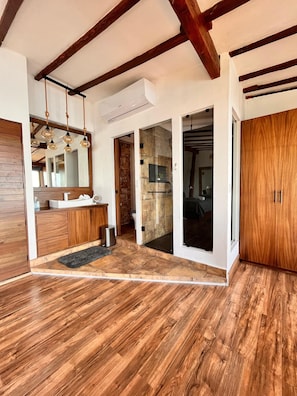 A spacious room with wooden flooring, a built-in wooden cabinet, a mirror, and a sliding glass door leading to another room.