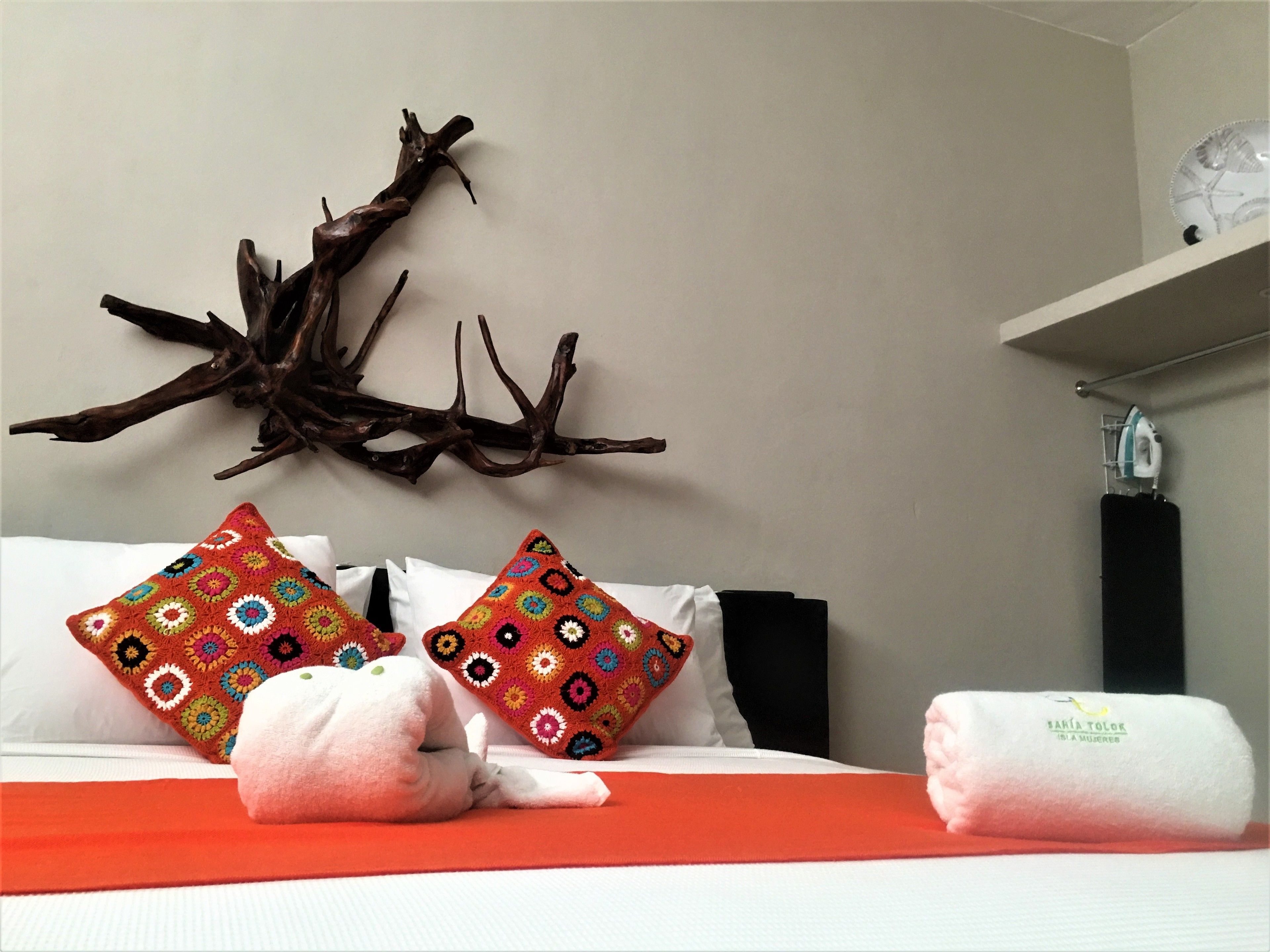 Habitación de hotel con cama, almohadas coloridas, una rama decorativa y una toalla al lado.