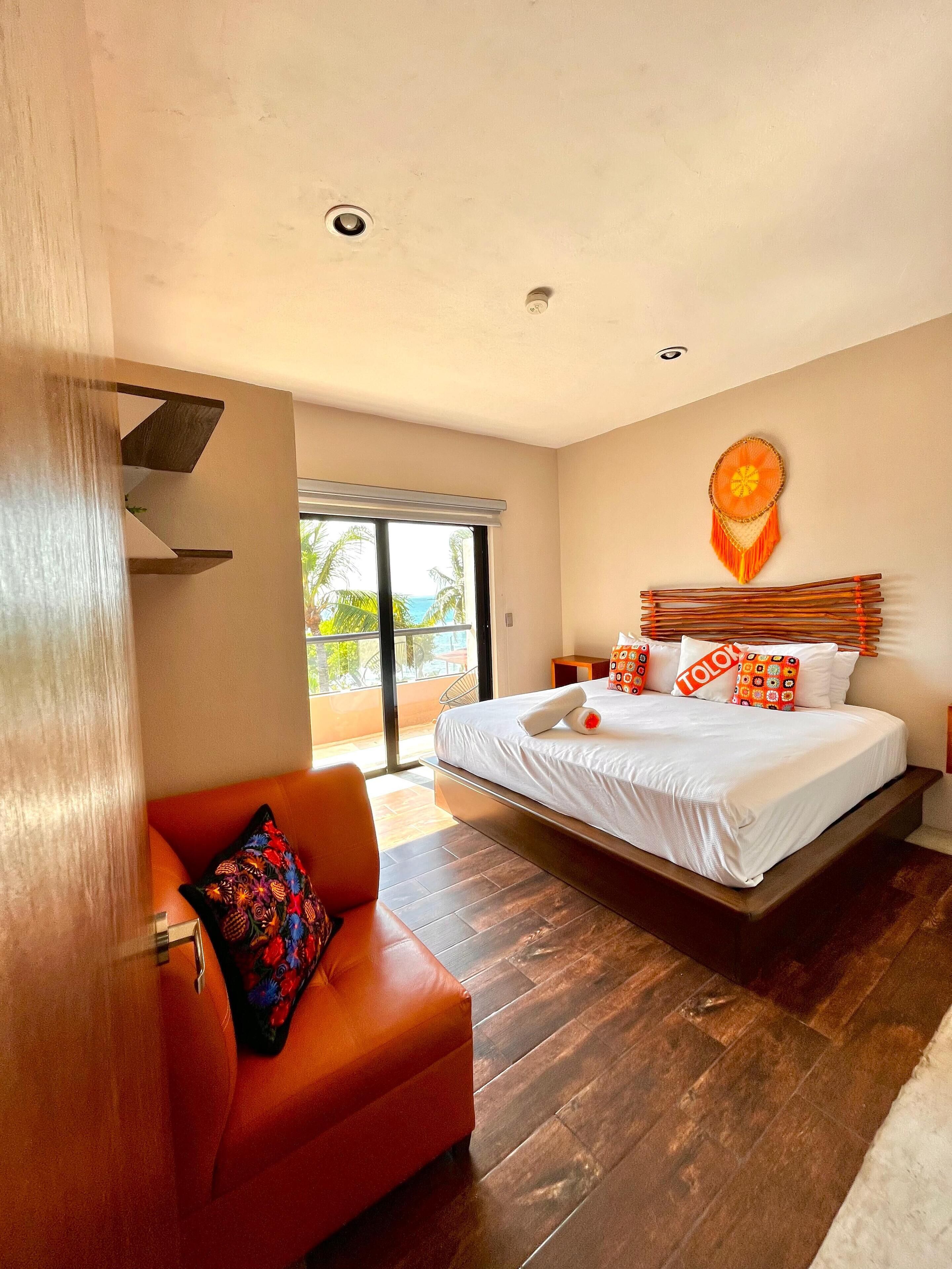 A modern hotel room with a large bed, a red sofa, and a view of the outdoors.