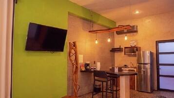A compact kitchen with a TV, bar area, and a refrigerator.