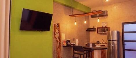 A compact kitchen with a TV, bar area, and a refrigerator.