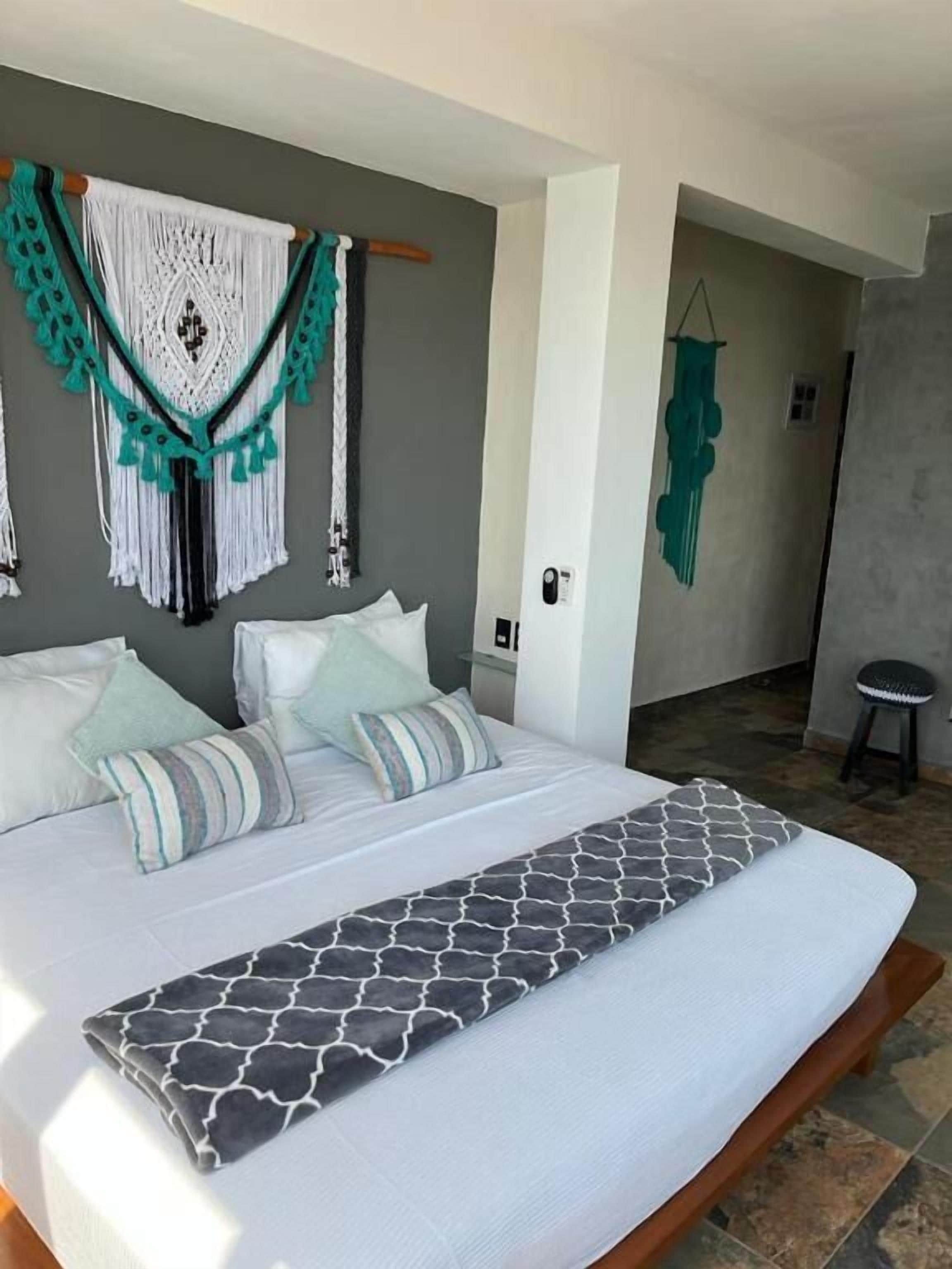 A bedroom with a large bed, a macrame wall hanging, and a small stool.