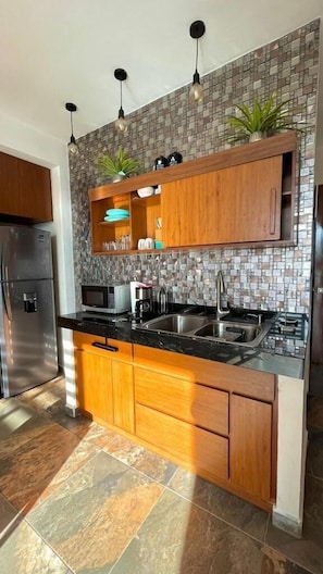 A modern kitchen with a granite countertop, stainless steel appliances, wooden cabinets, and a backsplash with mosaic tiles.