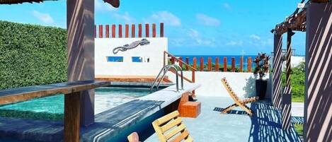 An outdoor swimming pool area with wooden loungers and a view of the ocean.