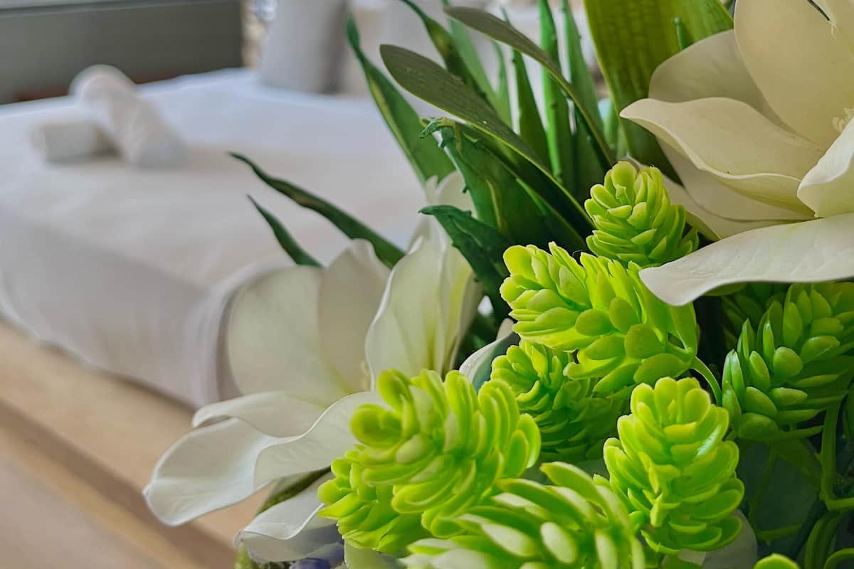 A modern bedroom with a bed, a bedside table, and a decorative plant arrangement.