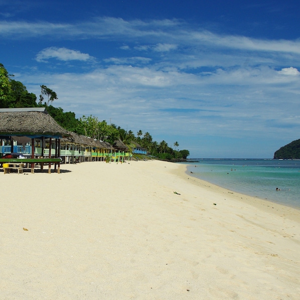A beach with thatched-roof huts and a clear blue sky.