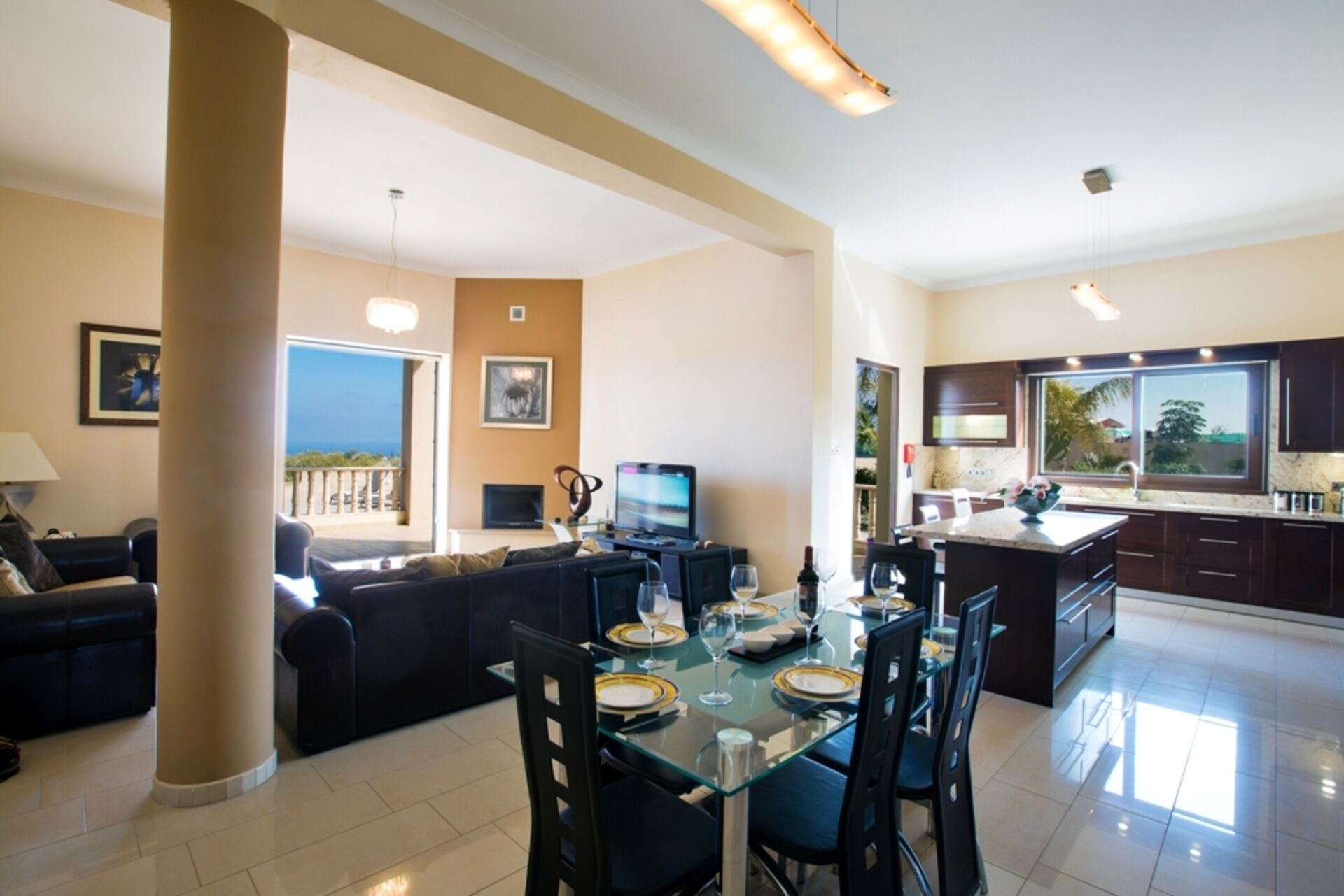 Un vaste espace de vie comprenant une table à manger pour quatre personnes, un canapé, un téléviseur et un balcon avec vue.