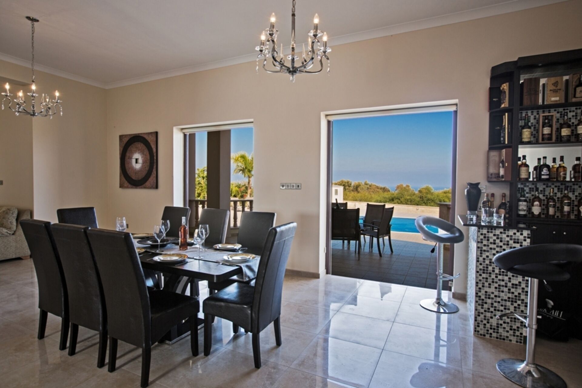 Un comedor con mesa dispuesta para cuatro, una barra con protector de salpicaduras de azulejos, y vistas a una piscina y al paisaje.