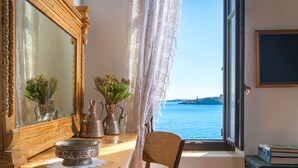A room with a wooden table, a chair, a mirror, and a view of the sea through a window. - Halki Sea House (Halki)