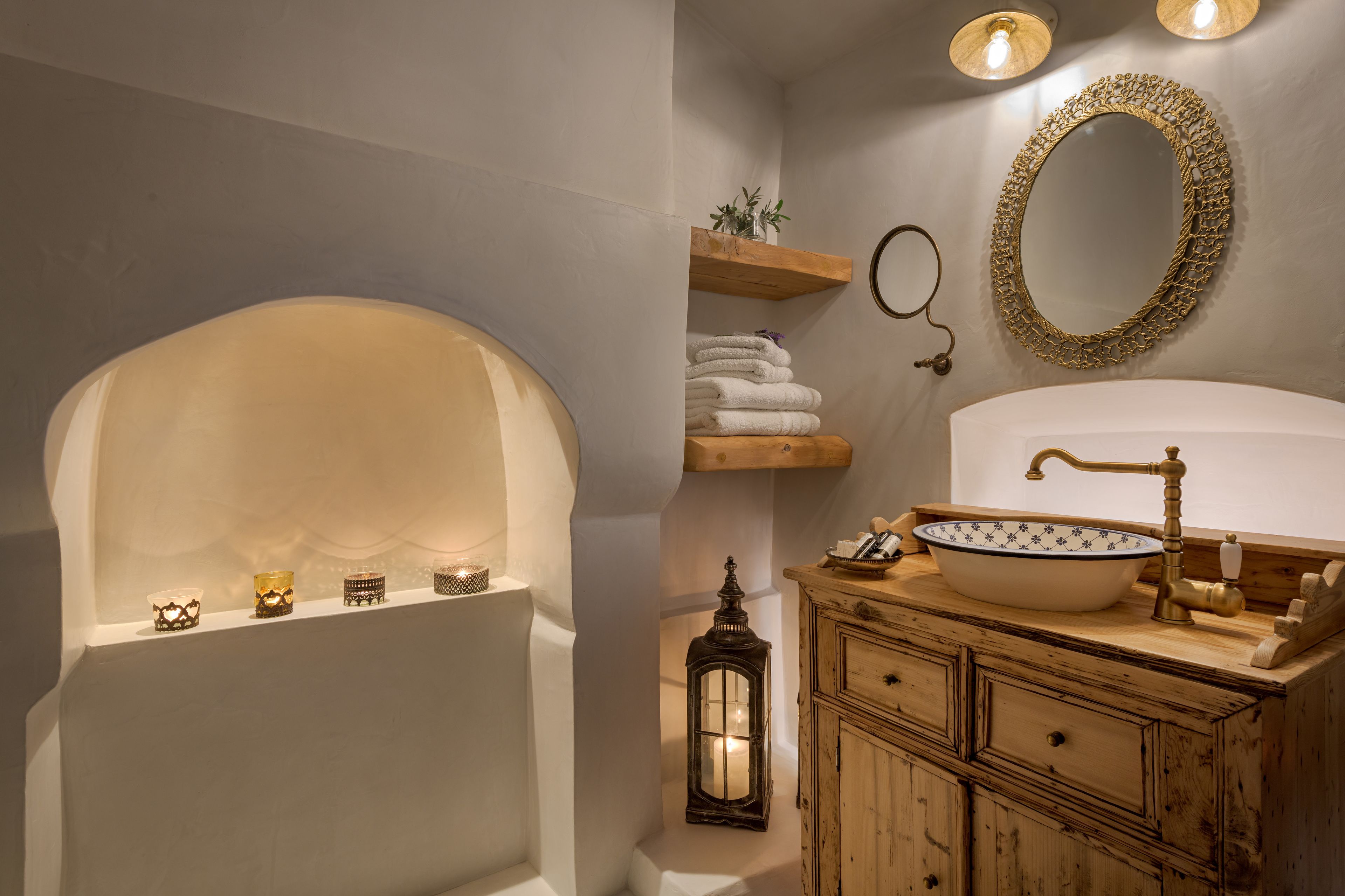 Un baño con bañera, un lavabo con un cuenco decorativo, un armario de madera, un espejo con marco dorado y un estante con toallas.