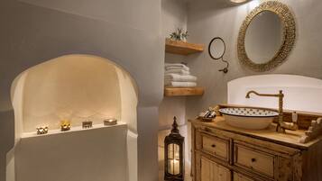 Un baño con bañera, un lavabo con un cuenco decorativo, un armario de madera, un espejo con marco dorado y un estante con toallas.