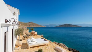 A balcony with a bed, lounge chairs, and a view of the sea. - Halki Sea House (Halki)