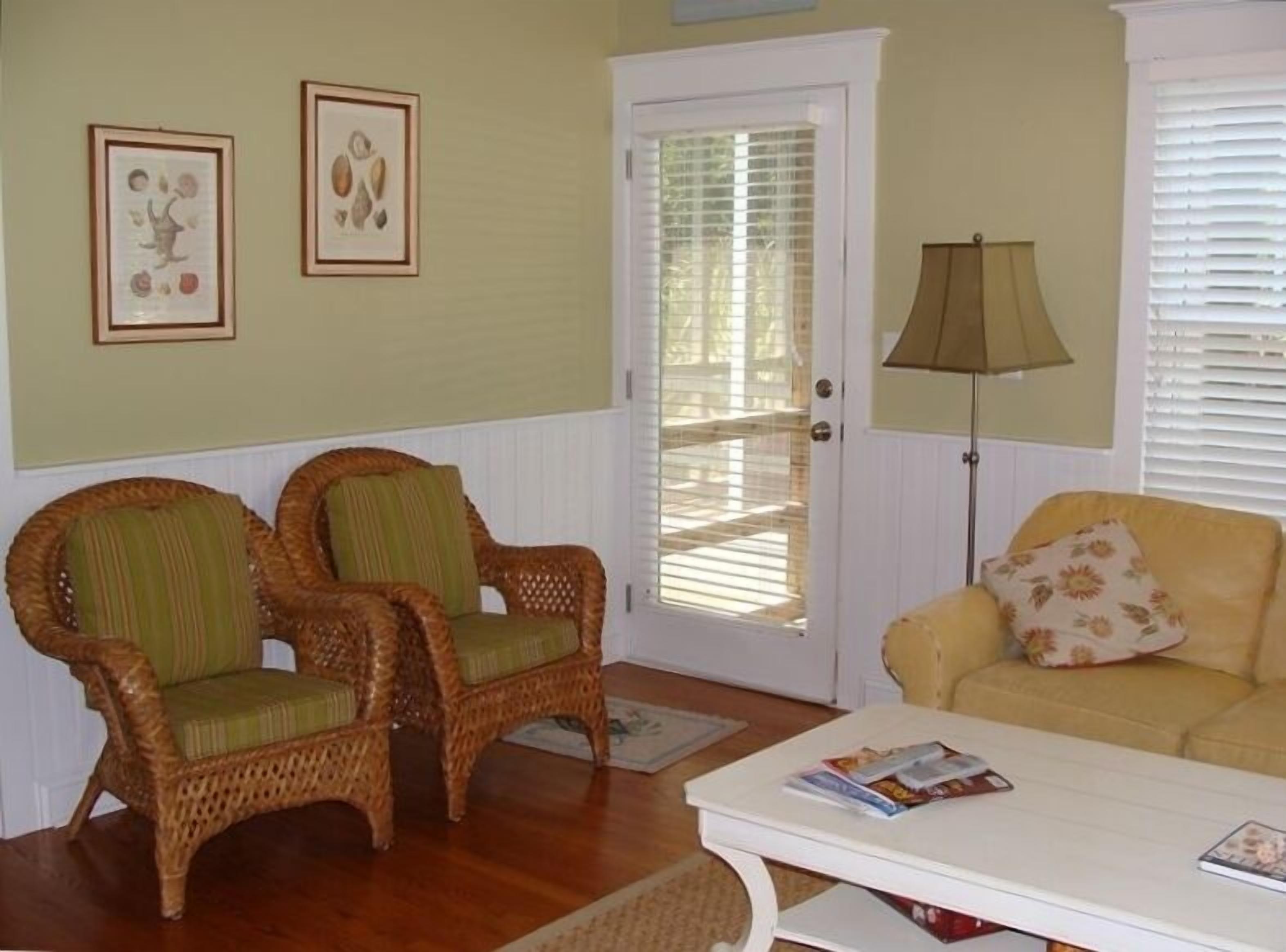 A room with two wicker chairs, a yellow sofa, a white coffee table, and a door with a window.