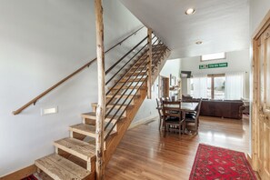 Un escalier en bois mène à une salle à manger agrémentée d’un tapis rouge et offrant une vue sur l’extérieur.