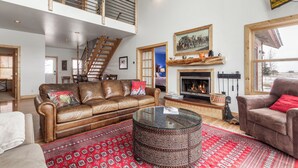 Un salón espacioso con techo alto, chimenea, escalera y un ventanal grande.
