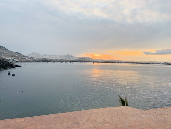 A calm waterfront with boats, a distant mountain range, and a clear sky.