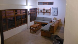 A cozy living room with a sofa, wooden coffee table, and a fireplace. There are large windows with wooden frames and a wall-mounted shelf with decorative items. - SECHIN HOUSE ,  ubicada en el Balneario de Tortugas Caleta Norte (Tortuga Casma)