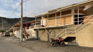 A building with a staircase leading to a second floor, a parked ATV, and a car in the background. - SECHIN HOUSE ,  ubicada en el Balneario de Tortugas Caleta Norte (Tortuga Casma)