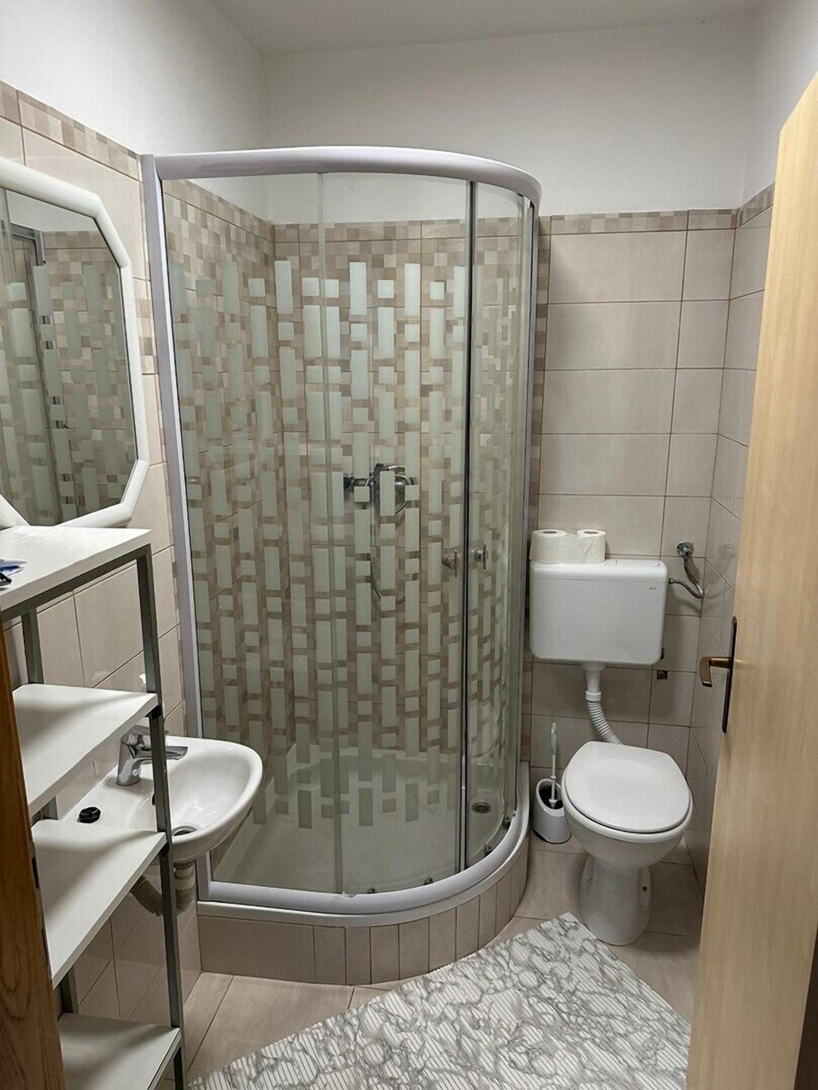 Ett badrum med en dusch som är avskärmad med glasväggar, en toalett och ett handfat med en spegel.