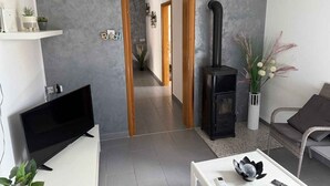 A modern living room with a black wood-burning stove, a flat-screen TV, and a white coffee table. - Holiday apartment with balcony (Šilo)