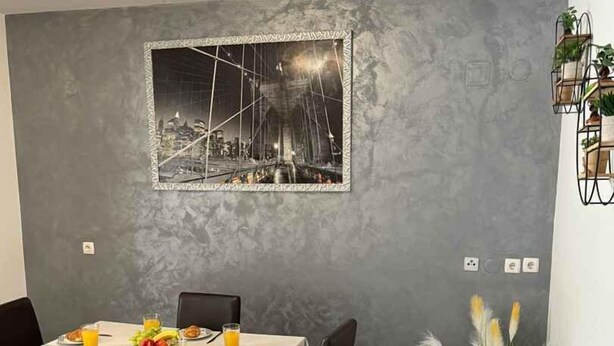 A dining area with a table set for two, a grey textured wall, and a framed picture above the table. - Holiday apartment with balcony (Šilo)
