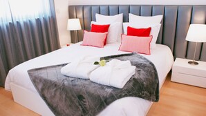 A neatly made bed with white and red pillows, a marble throw blanket, and a folded towel with a flower. - Ana's Apartments, Sea View (Sines)