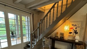A spacious room with a tiled floor, a staircase with a wooden railing, and a large window with a view of greenery outside.