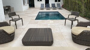A pool area with wicker furniture and a tiled floor.