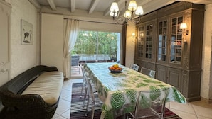 A dining area with a table set for four, a wicker sofa, and a view of greenery outside.