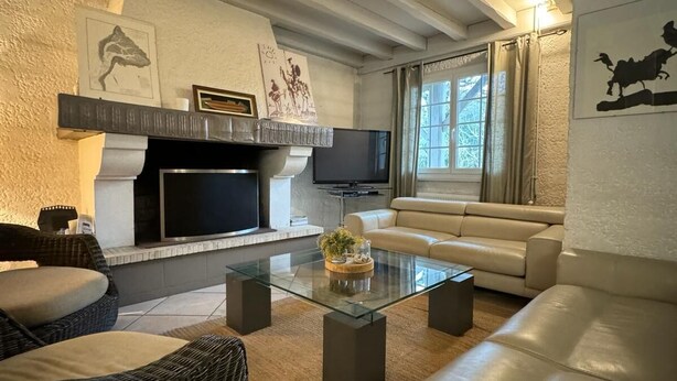 A modern living room with a fireplace, leather sofas, a glass coffee table, and artwork on the walls.