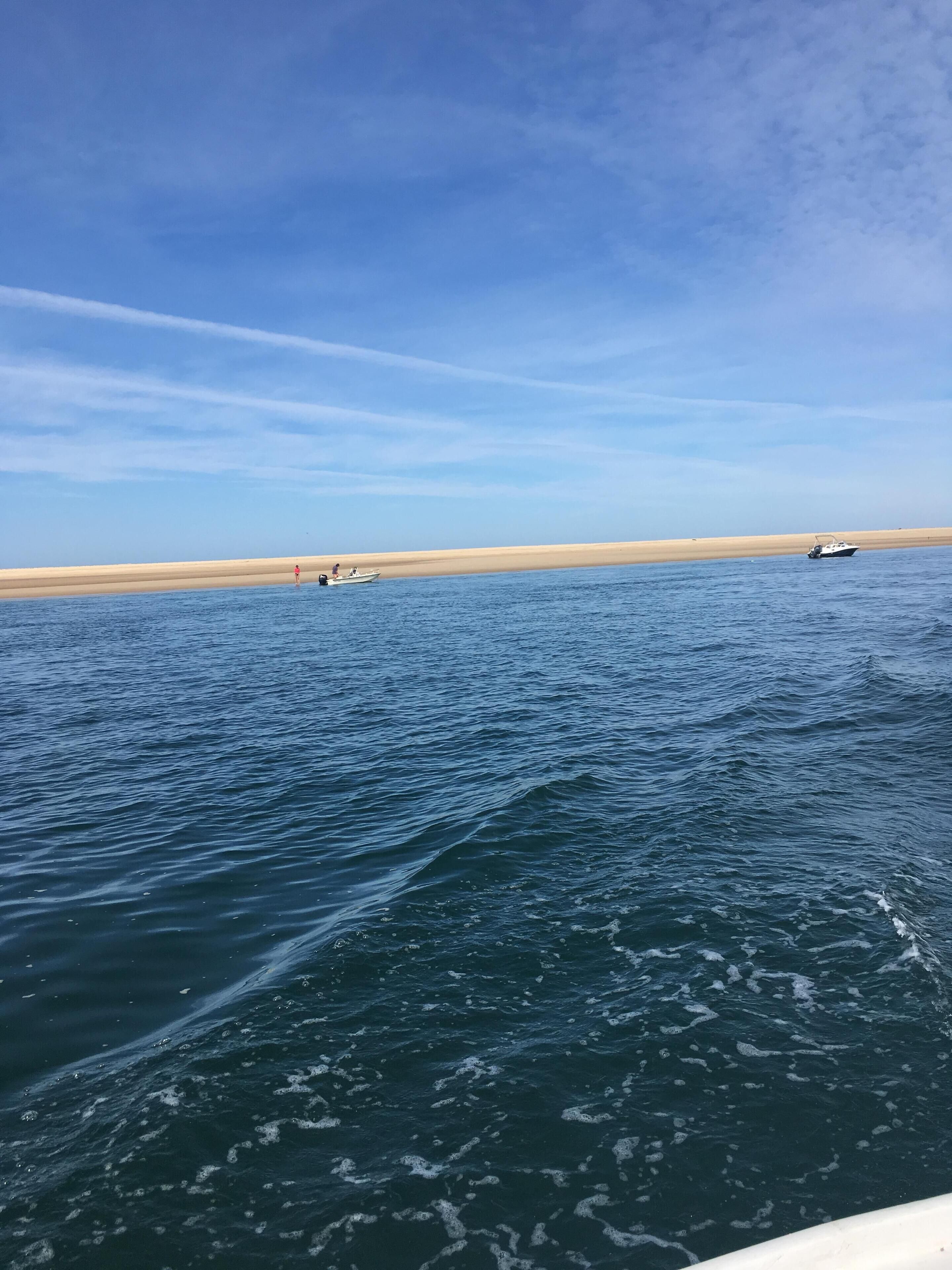 A view of a calm sea with boats and a sandy beach in the distance.