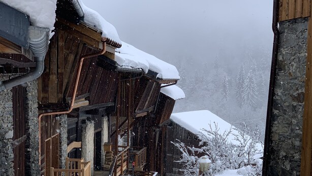 A wooden building with a staircase leading to a porch, surrounded by snow-covered ground and trees.