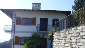 A two-story building with a stone wall and a balcony. - Holiday home in southern gardens with breathtaking panoramic views  (Canobio/Carmine)