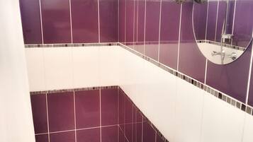 A bathroom with purple and white tiles, a white sink, and a shower with a wooden branch decoration.