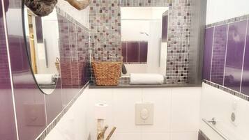 A small bathroom with a white sink, a toilet, and a mirror. There is a decorative branch and a woven basket on the counter.