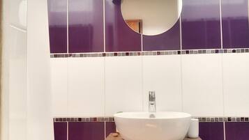 A bathroom with a white sink, purple tiles, a wooden vanity, and a mirror with a branch decoration.
