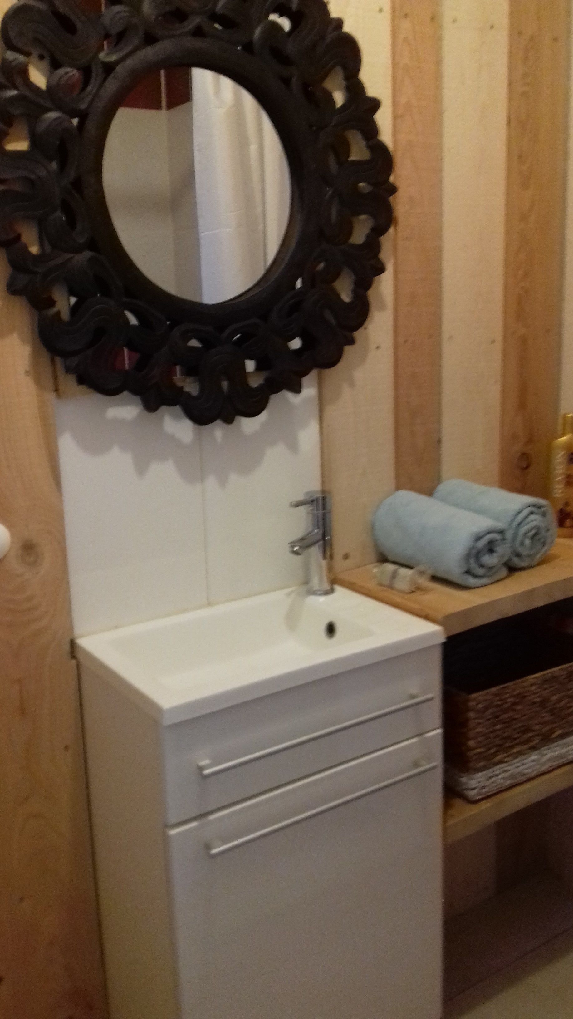 A bathroom with a white sink, a mirror with an ornate black frame, and a wooden vanity with a towel rack holding two rolled towels.