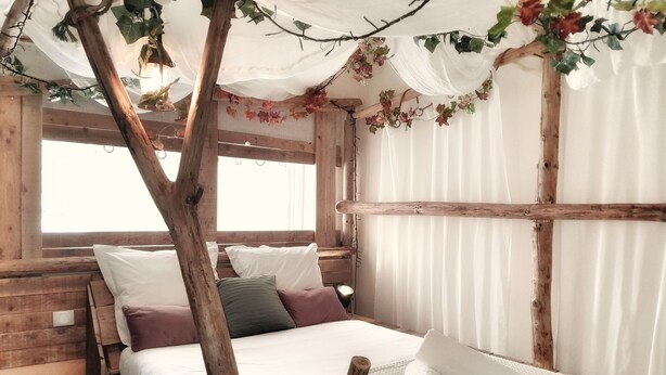 Une pièce chaleureuse en bois, avec un lit, des oreillers et un baldaquin.
